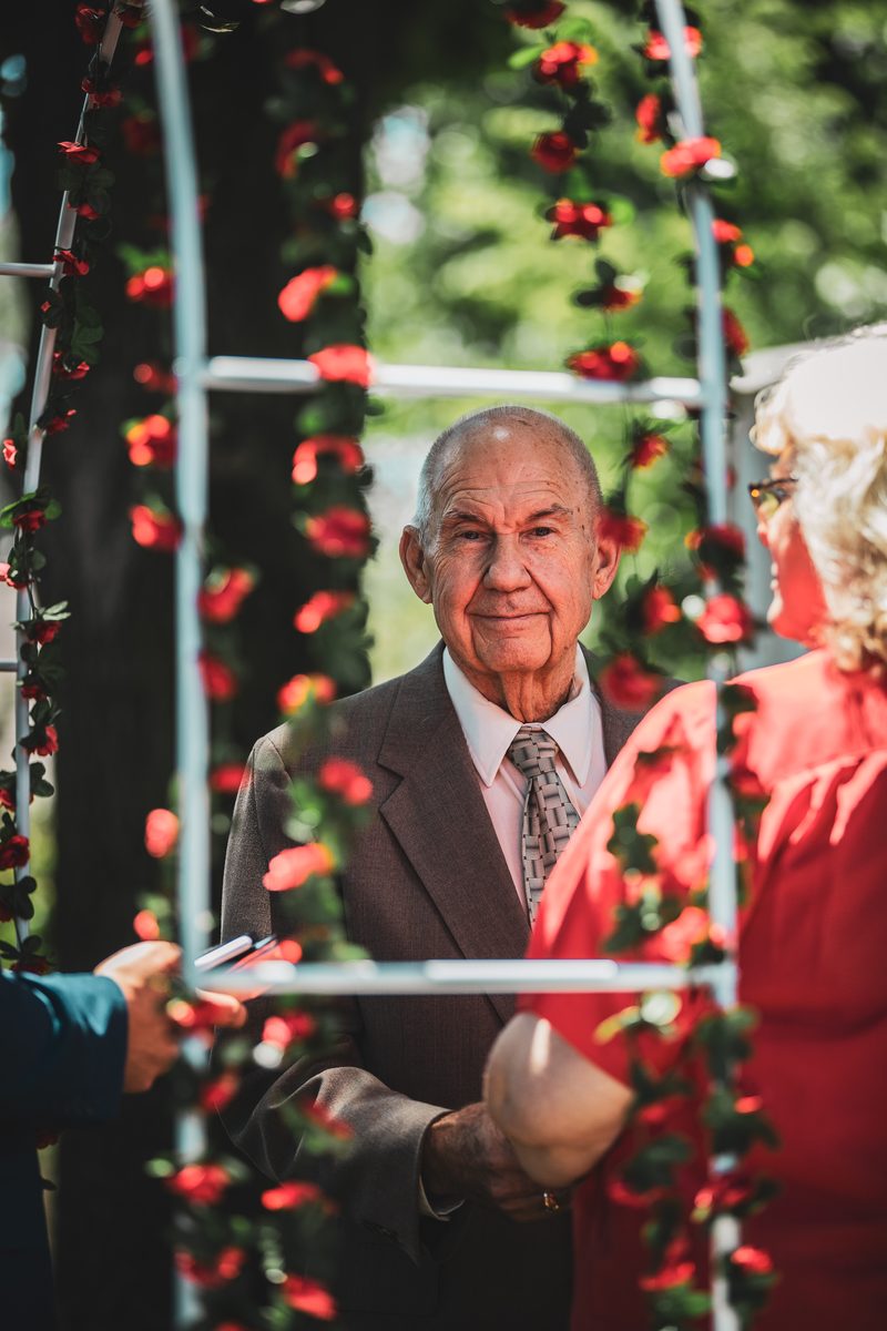 Elderly groom in a suit standing under a floral arch