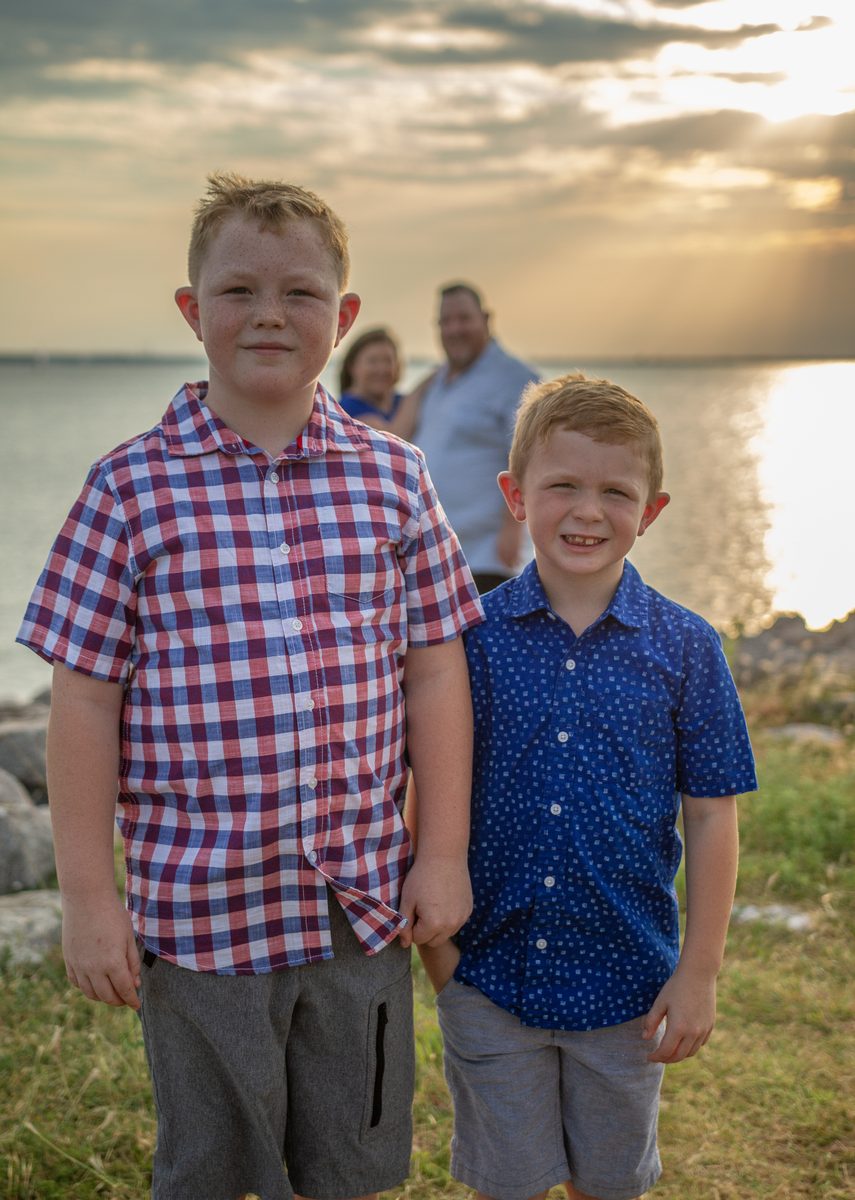 Two brothers smiling at sunset with family in the background