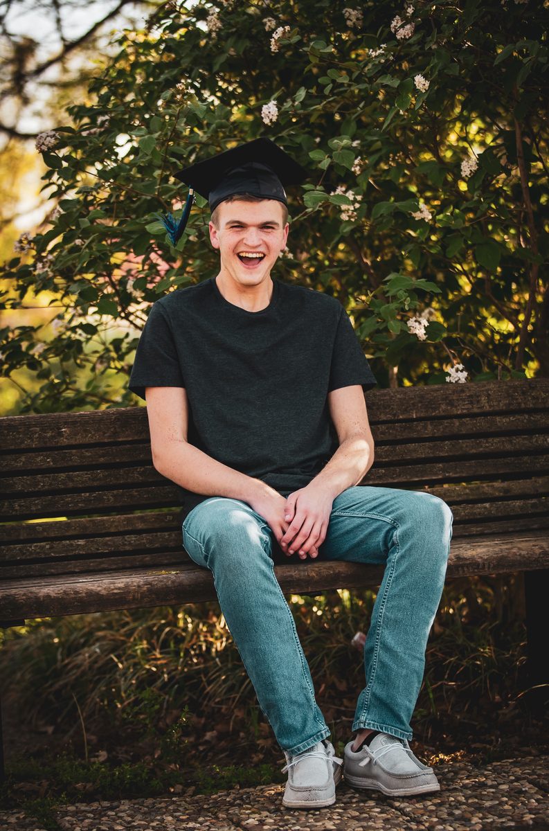 Graduating senior laughing while wearing his cap on a park bench